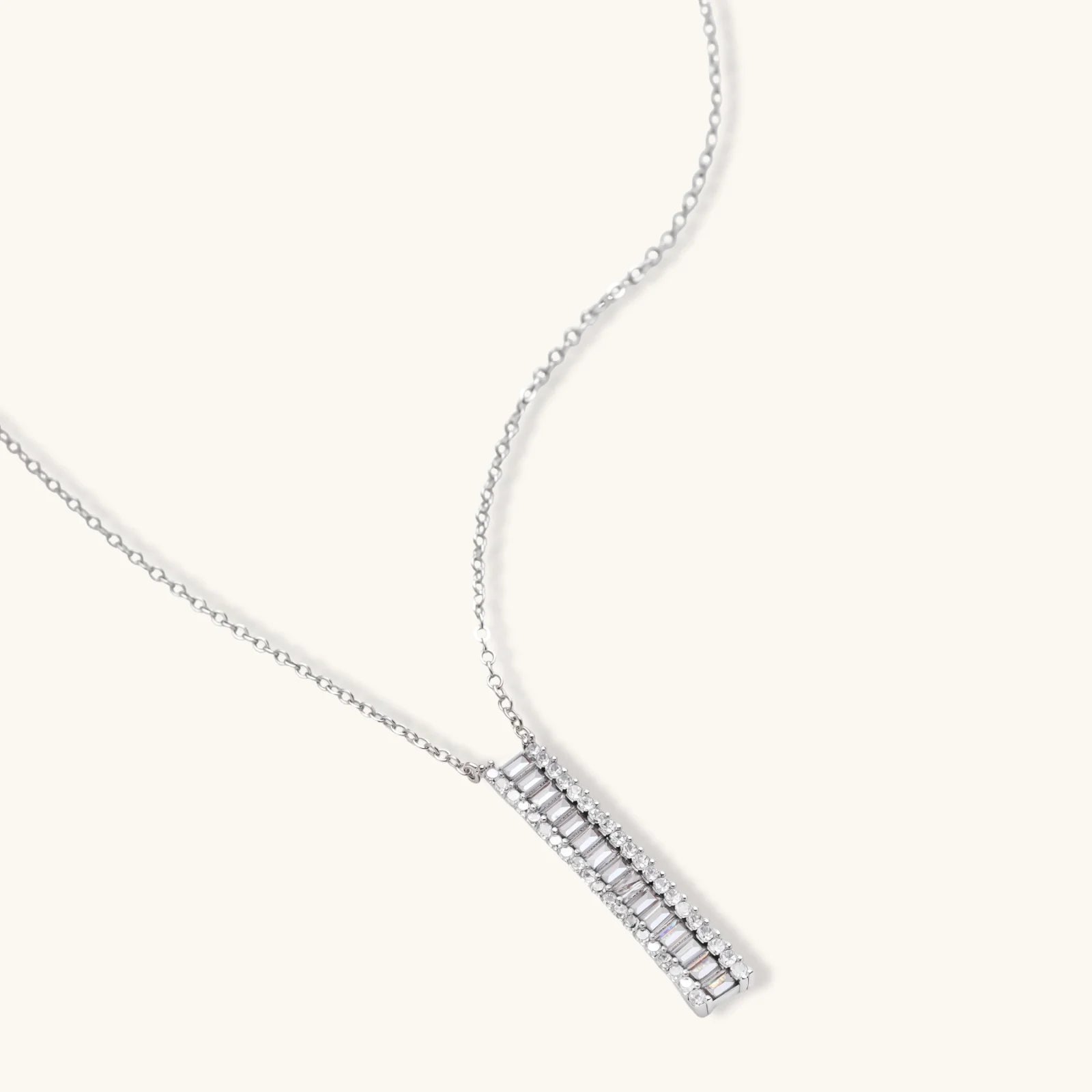 White gold plated necklace with vertical cubic zirconia pendant and matching hoop earrings on neutral background