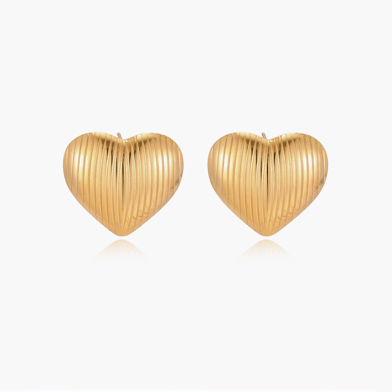 Gold heart-shaped stud earrings with parallel ridged texture on cream background
