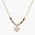 Gold-toned beaded necklace with grey stones and quatrefoil abalone shell pendant on cream background.