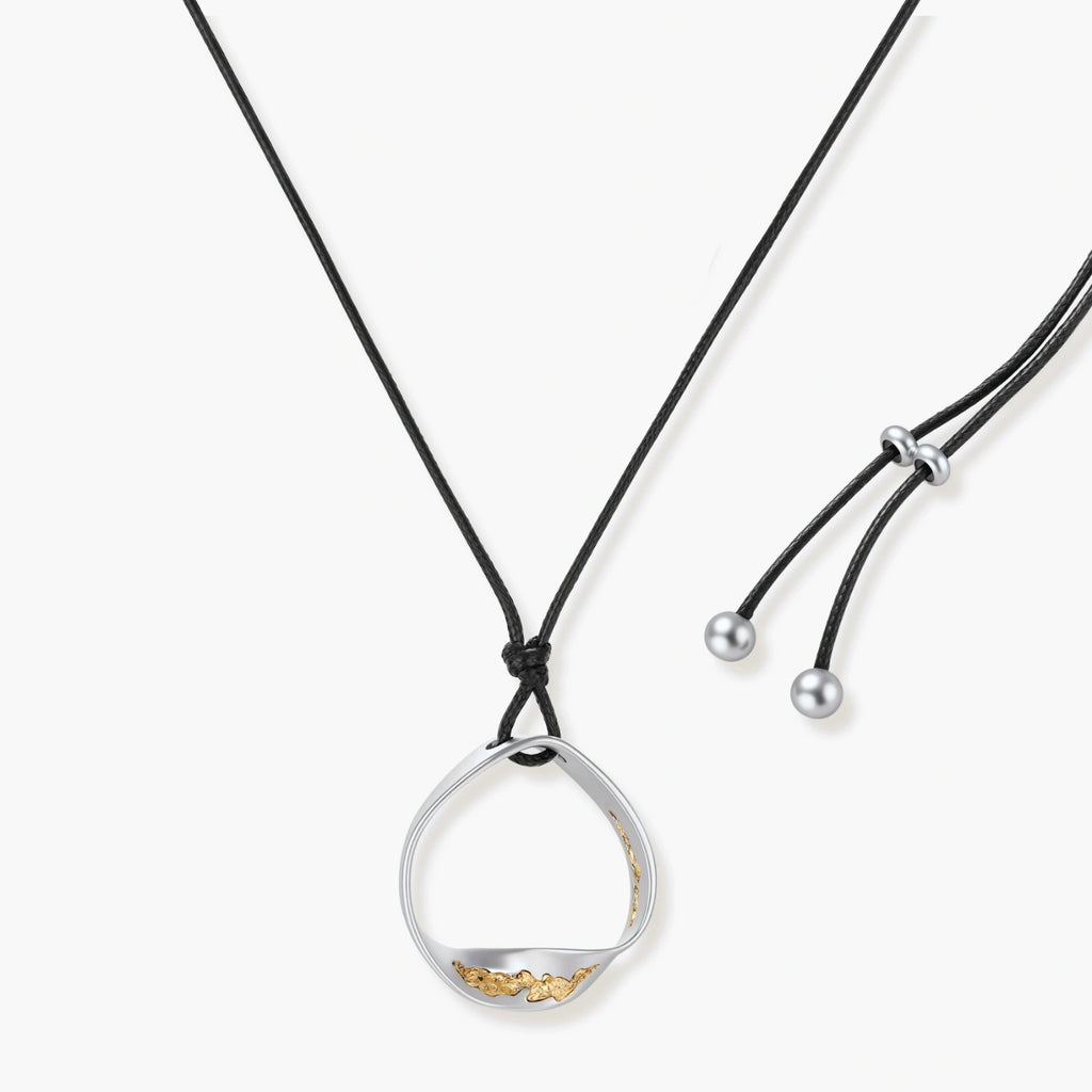 Artistic jewelry set featuring curved silver pendant with gold veining on black cord plus matching asymmetrical hoop earrings