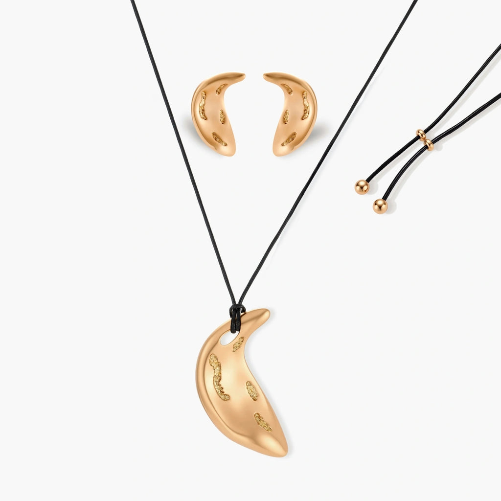Gold-toned crescent moon pendant with textured surface on black adjustable cord, displayed with matching crescent earrings