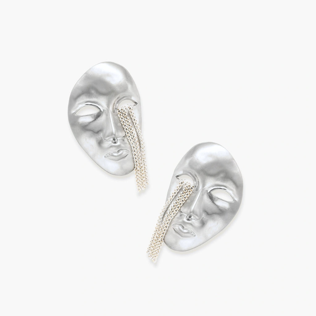Silver face-shaped statement earrings with flowing chain tassels hanging from sculpted lips on cream background