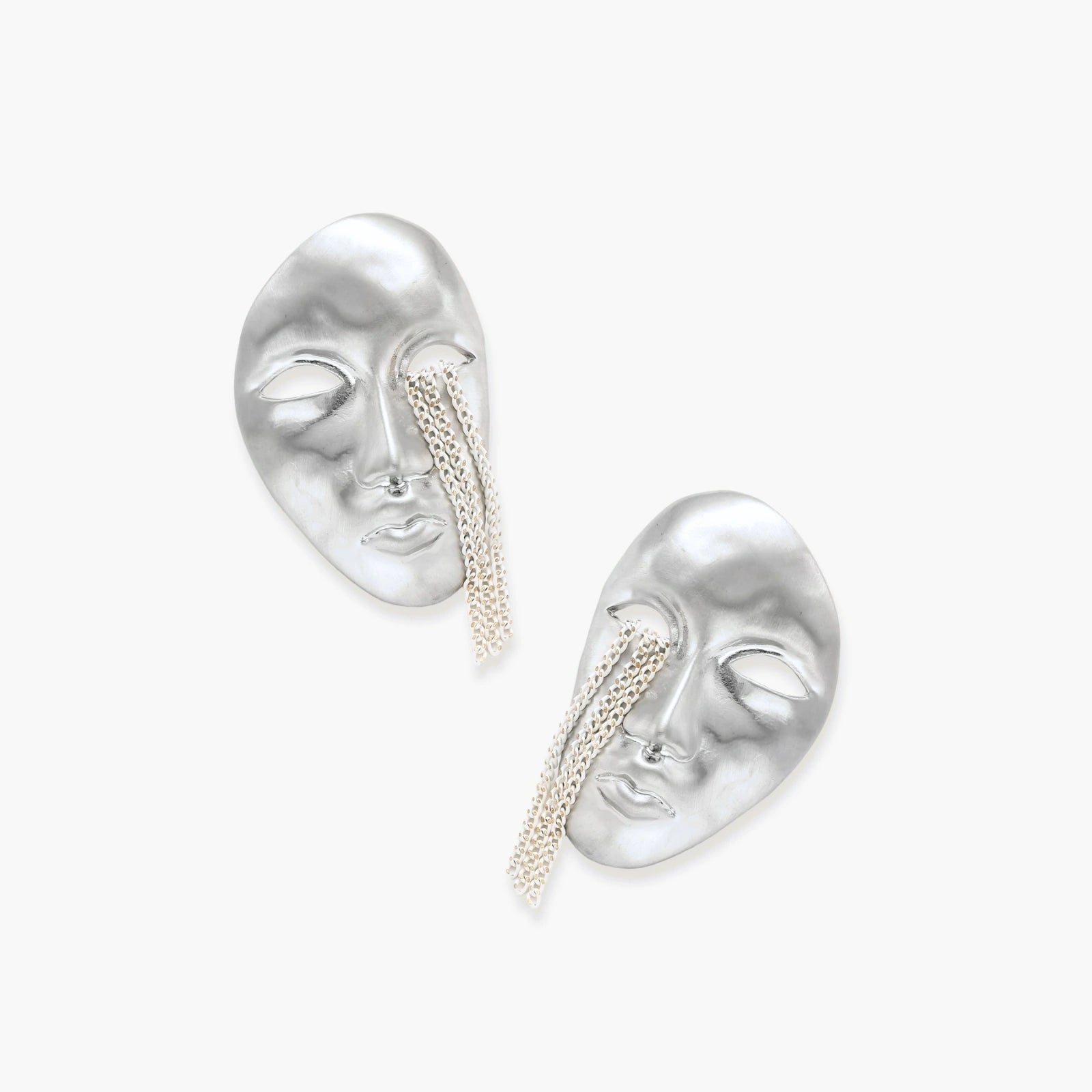 Silver face-shaped statement earrings with flowing chain tassels hanging from sculpted lips on cream background