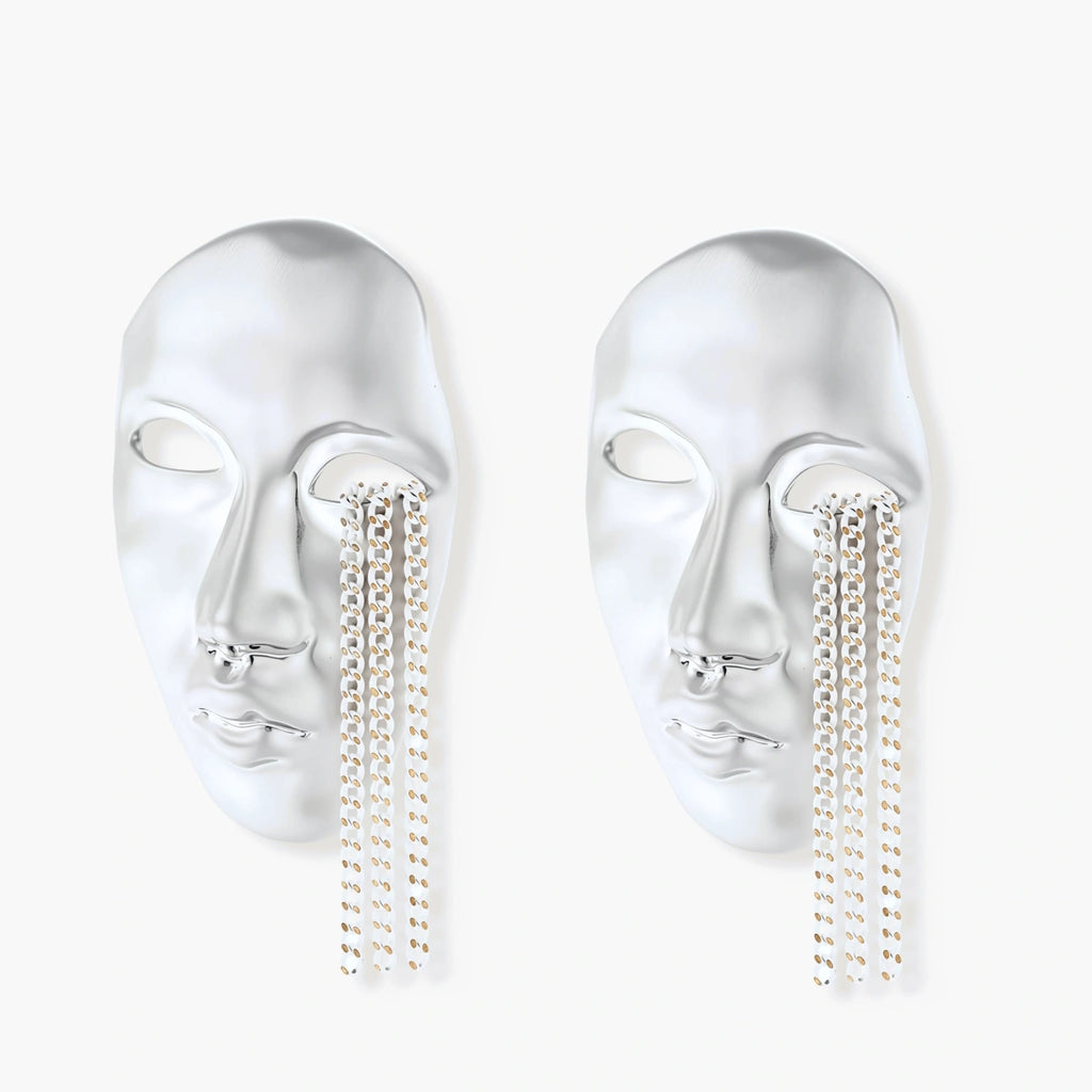 Silver face-shaped statement earrings with flowing chain tassels hanging from sculpted lips on cream background