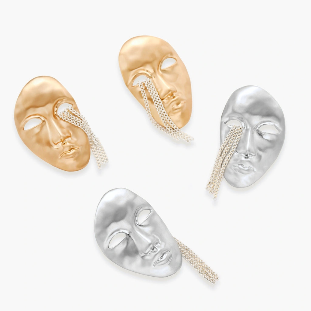Silver face-shaped statement earrings with flowing chain tassels hanging from sculpted lips on cream background